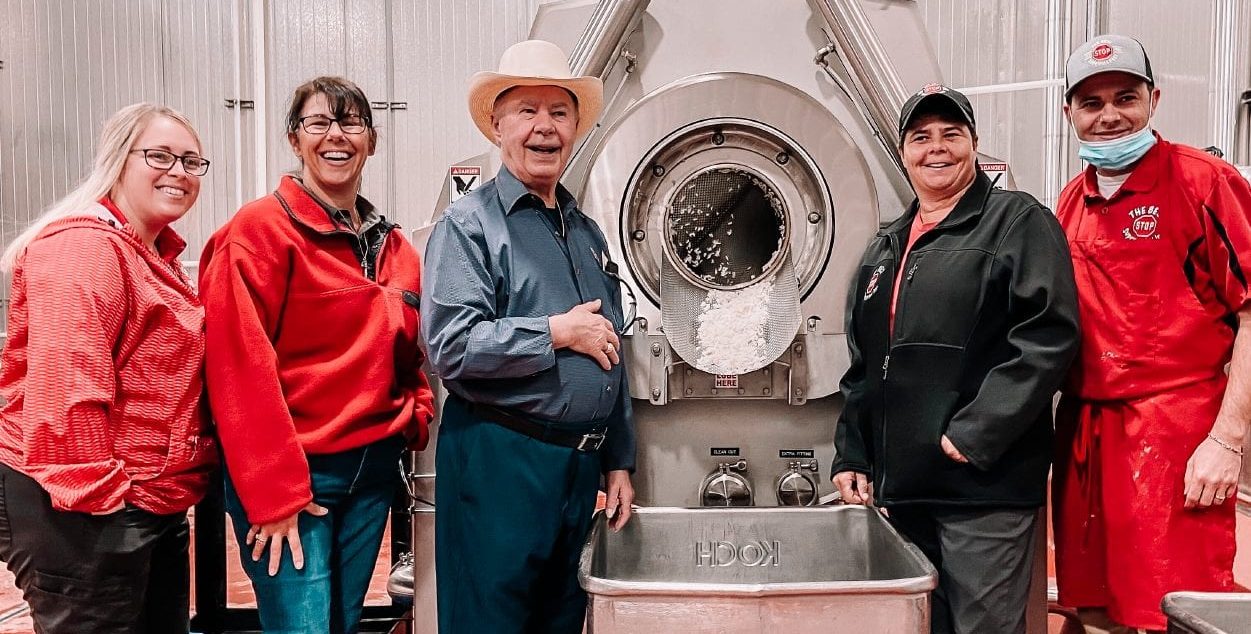 photo of best stop family standing in front of industrial food processor inside of the best stop wholesale facility