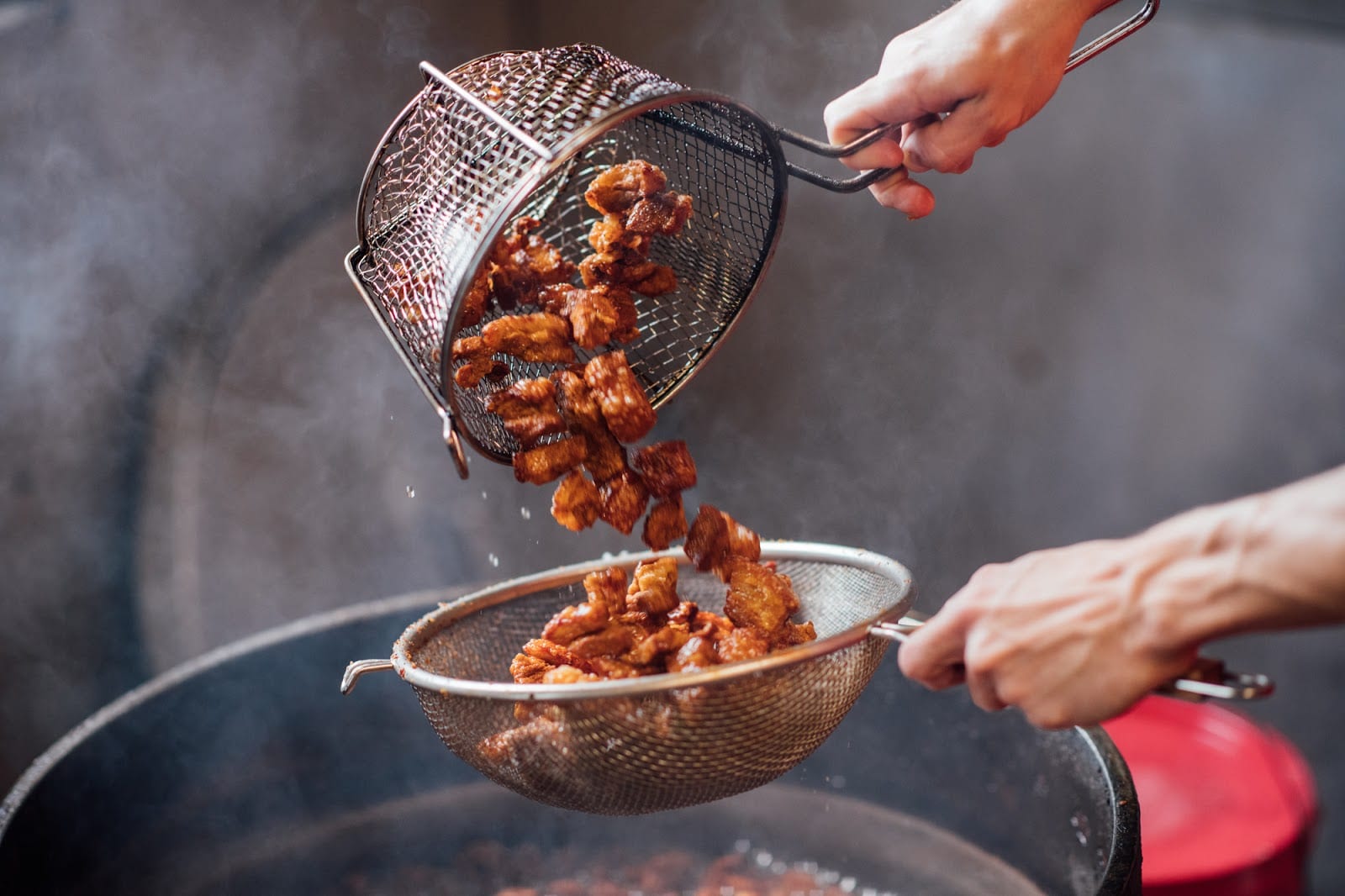 cracklins being poured into strainer above cast iron wash pot